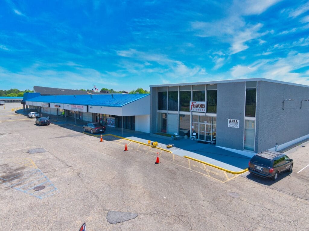 Exterior view of Normendale Shopping Center featuring storefronts and parking area under clear blue sky.