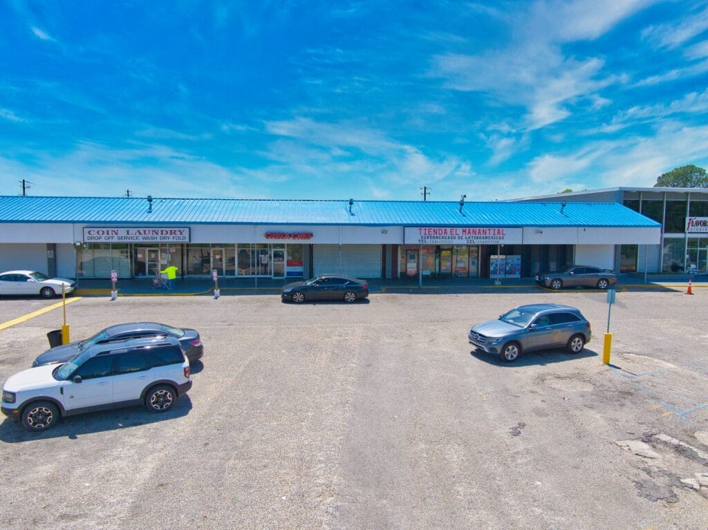 A modern shopping center with various storefronts and a clear blue sky, showcasing the Normendale Shopping Center.